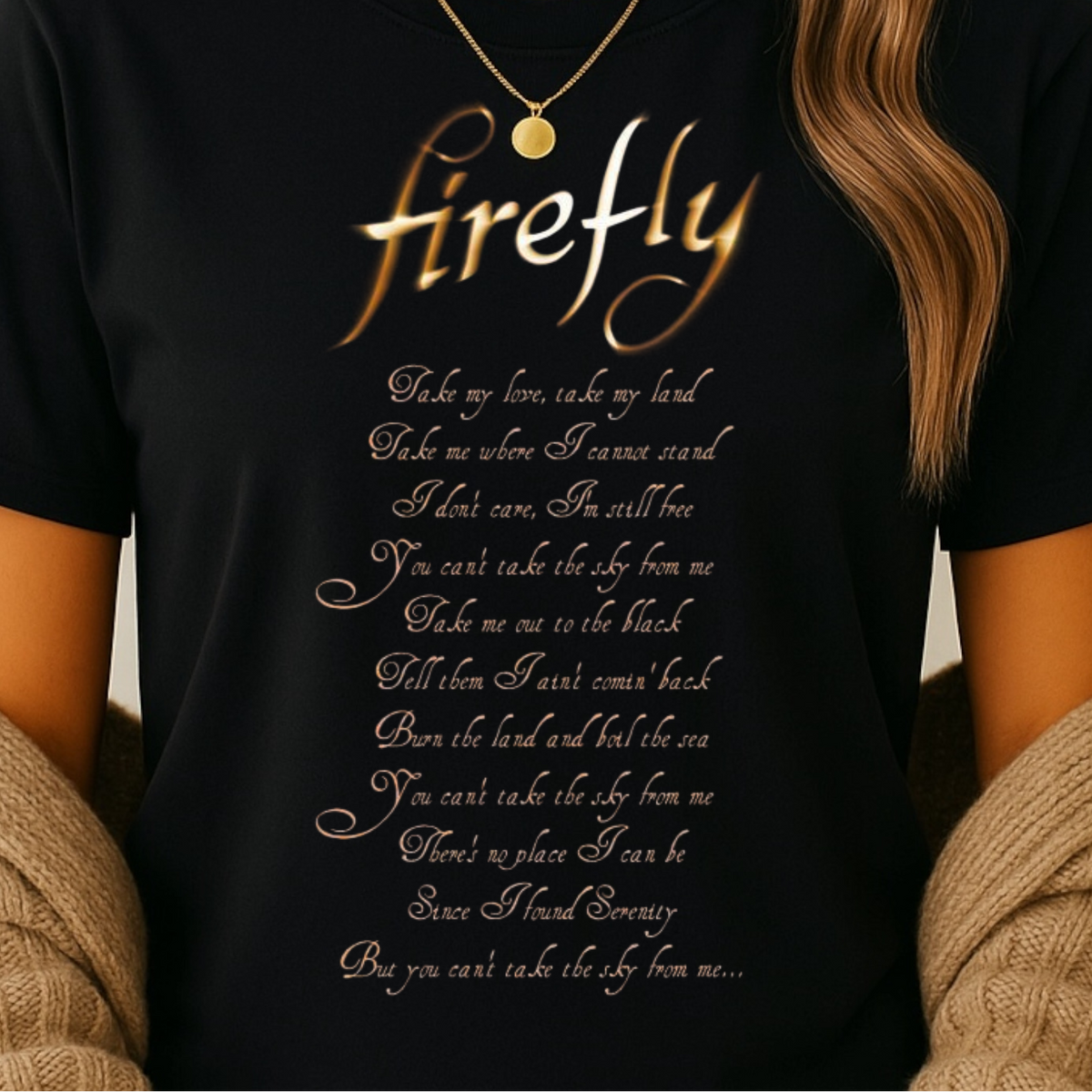 A woman wearing a black short-sleeve graphic T-shirt with the word 'firefly' in large metallic gold script and a poem printed below in small gold text. She is also wearing a beige knit cardigan and a gold necklace, photographed against a plain light background.