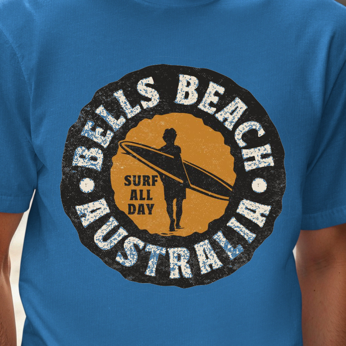 A man wearing a bright blue t-shirt with a circular 'Bells Beach Australia Surf All Day' graphic on the chest, set against a blurred city street background.