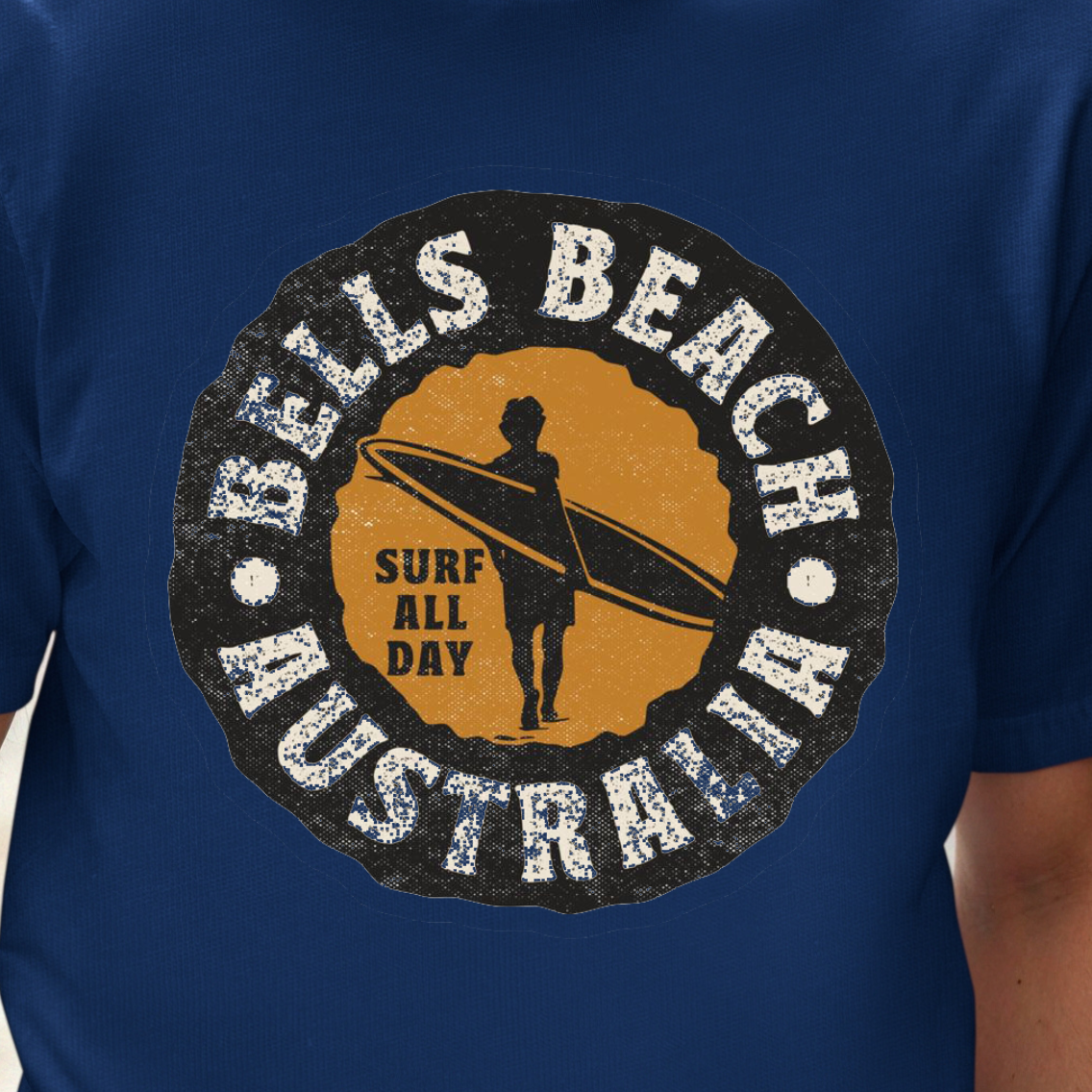 A man wearing a royal blue t-shirt with a circular 'Bells Beach Australia Surf All Day' graphic on the chest, set against a blurred city street background.