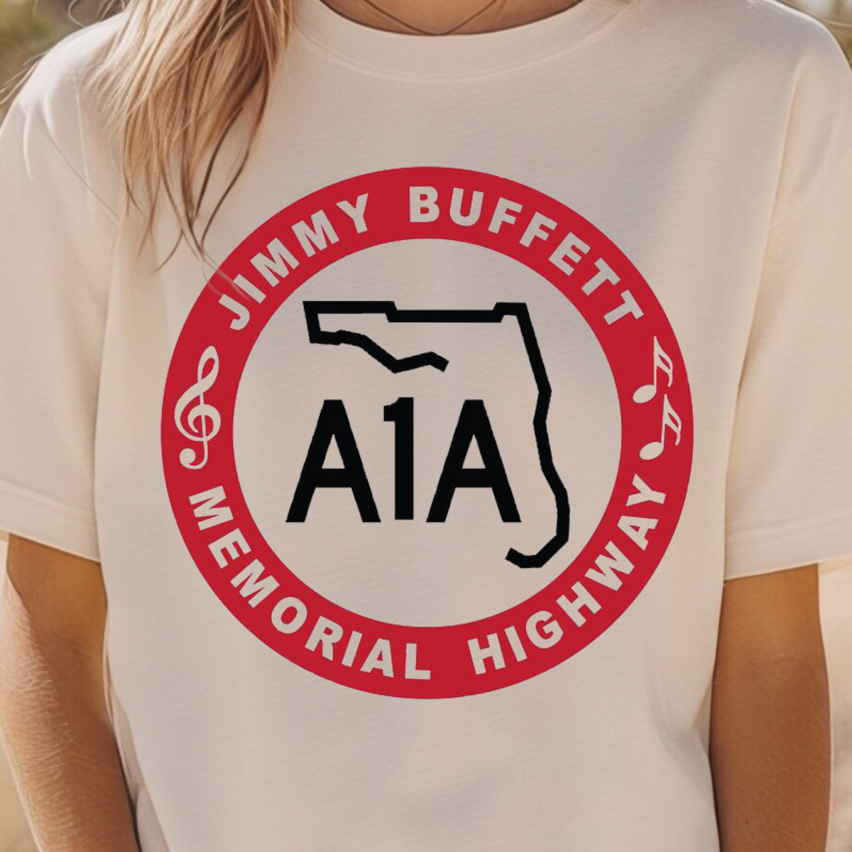 A person wearing a cream-colored t-shirt with a red and black circular graphic that reads 'JIMMY BUFFETT MEMORIAL HIGHWAY A1A' with a Florida state outline.