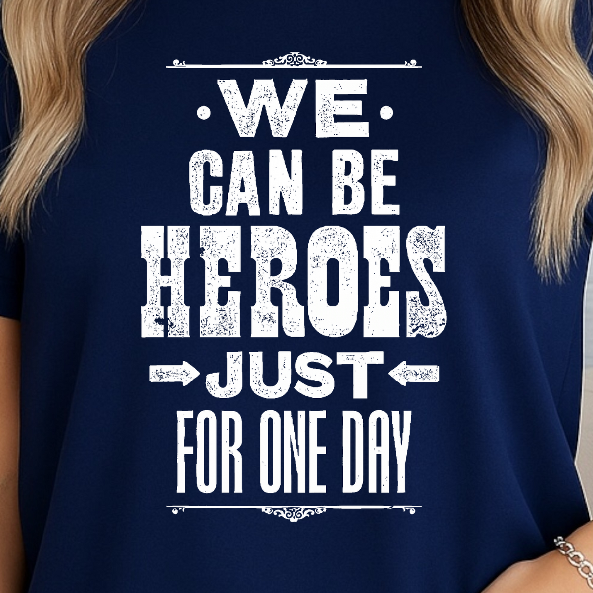 A woman wearing a navy blue short-sleeve t-shirt with a distressed white graphic that reads 'WE CAN BE HEROES JUST FOR ONE DAY'.