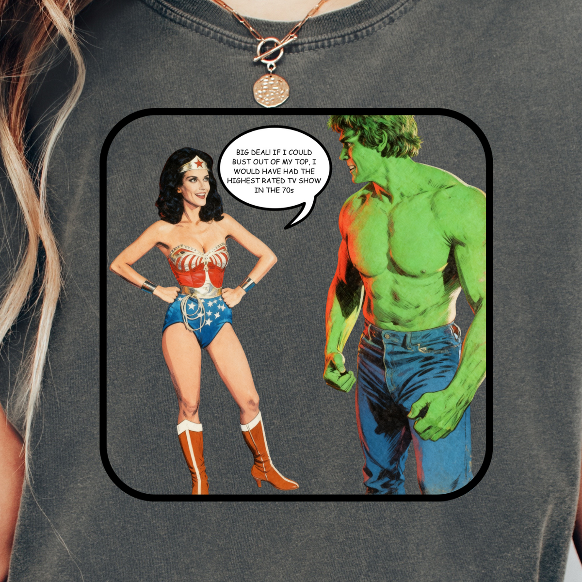 A woman wearing a dark gray graphic t-shirt featuring a comic-style print of Wonder Woman and the Hulk with a speech bubble.